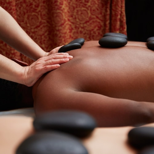 Someone getting a hot stone massage with a stone on each side of their spine.  The therapist is pressing on their shoulders.
