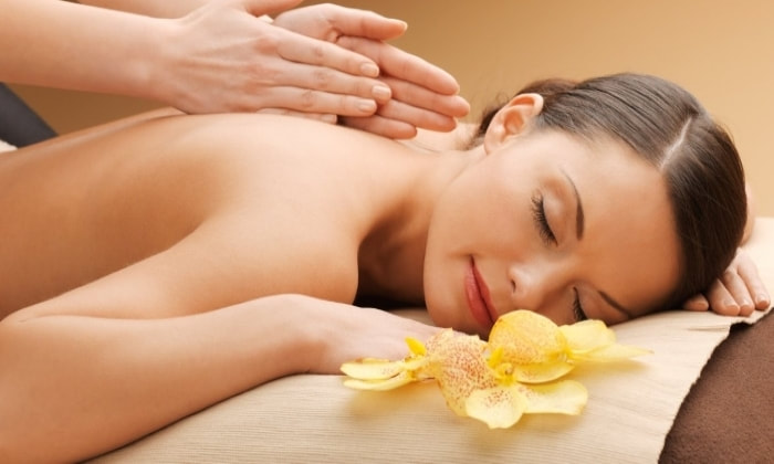 A lady lying on a massage table while a therapists hands are using the tapotement massage technique.  There is a yellow flower next to the ladies head.  It appears she is getting a Swedish massage.