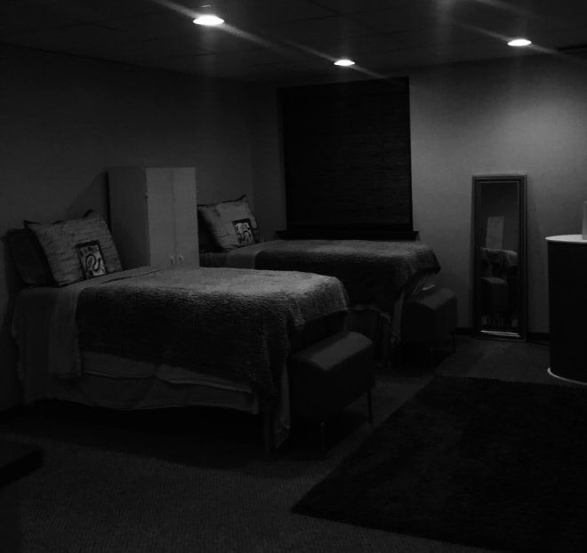 This is a picture of a massage room at CM Massotherapy in Erie, PA.  There are two massage tables draped with white sheets.  There is a beautiful window in the picture with a massive mirror right next to it.