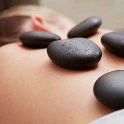 Lady with dark blonde hair getting a hot stone massage with hot stones on each side of her spine.